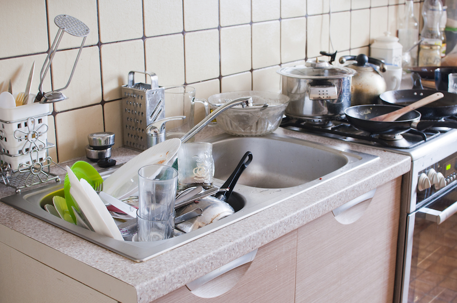 Une cuisine avec un évier rempli de vaisselle salle et des plaques de cuisson avec des plats en train de chauffer