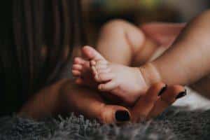 une jeune maman tient les pieds de son bébé dans sa main.
