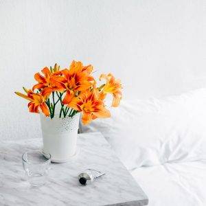 bouquet de fleurs orange dans une chambre, sur une table de chevet en marbre, des draps et un mur blancs