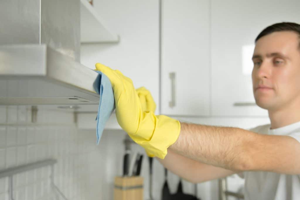Un homme de ménage nettoyant une hotte de cuisine à l'aide d'un chiffon en tissu