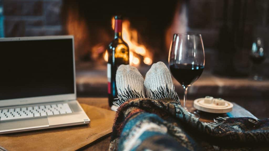 Personne cozy près d'un feu de cheminée, sous un plaid avec un ordinateur et un verre de vin rouge
