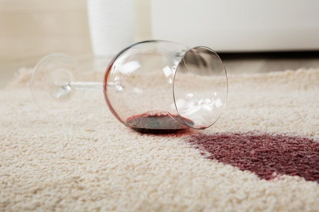 un verre de vin rouge renversé sur un tapis blanc, créant une grosse tache de vin rouge