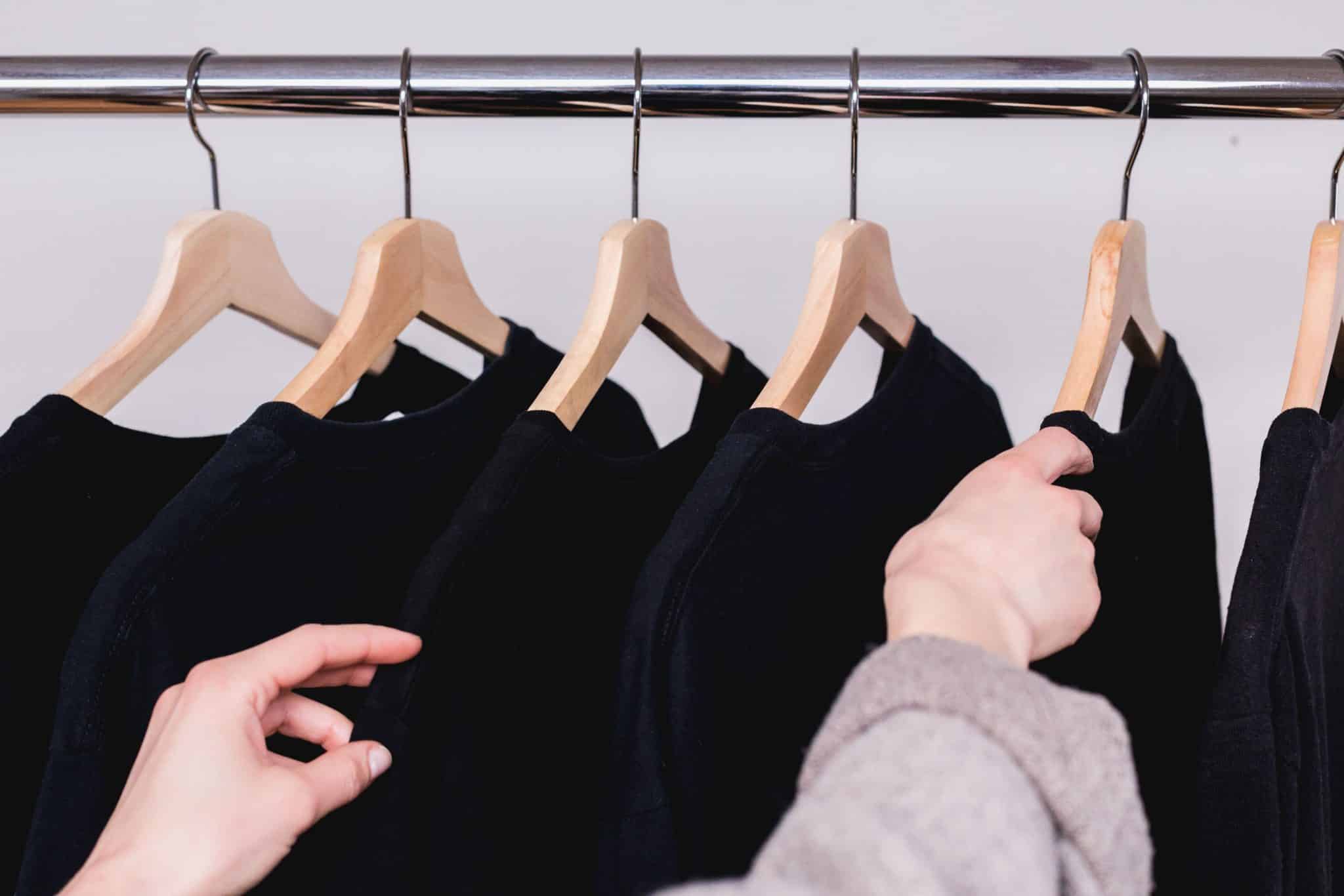 Une femme choisit parmi plusieurs vêtements noirs sur des cintres.