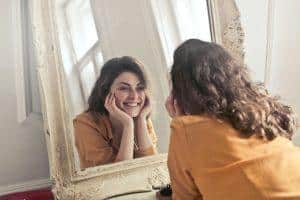 une femme qui souris à son reflet dans le miroir